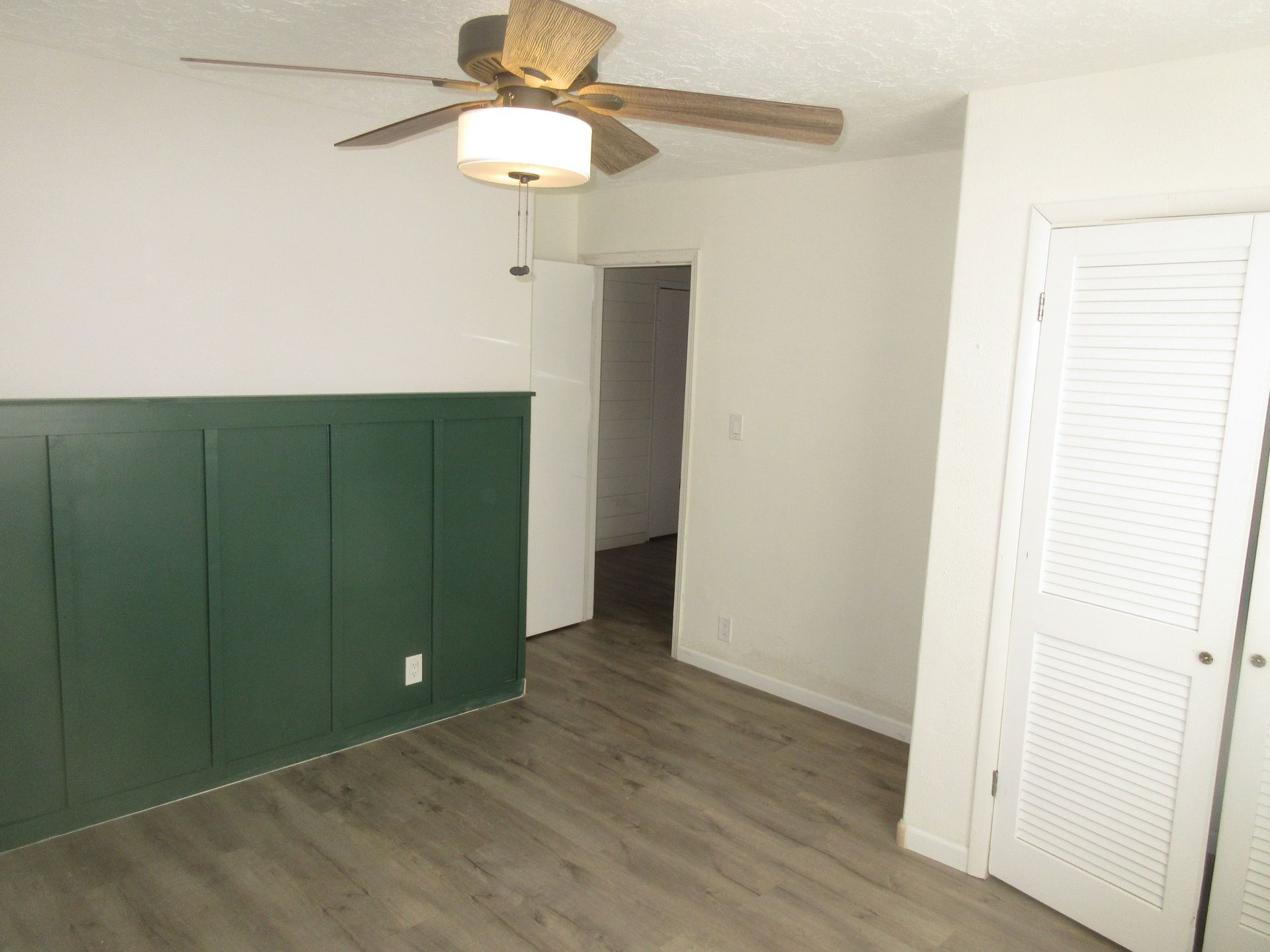 There is a ceiling fan in the room with a green wall.