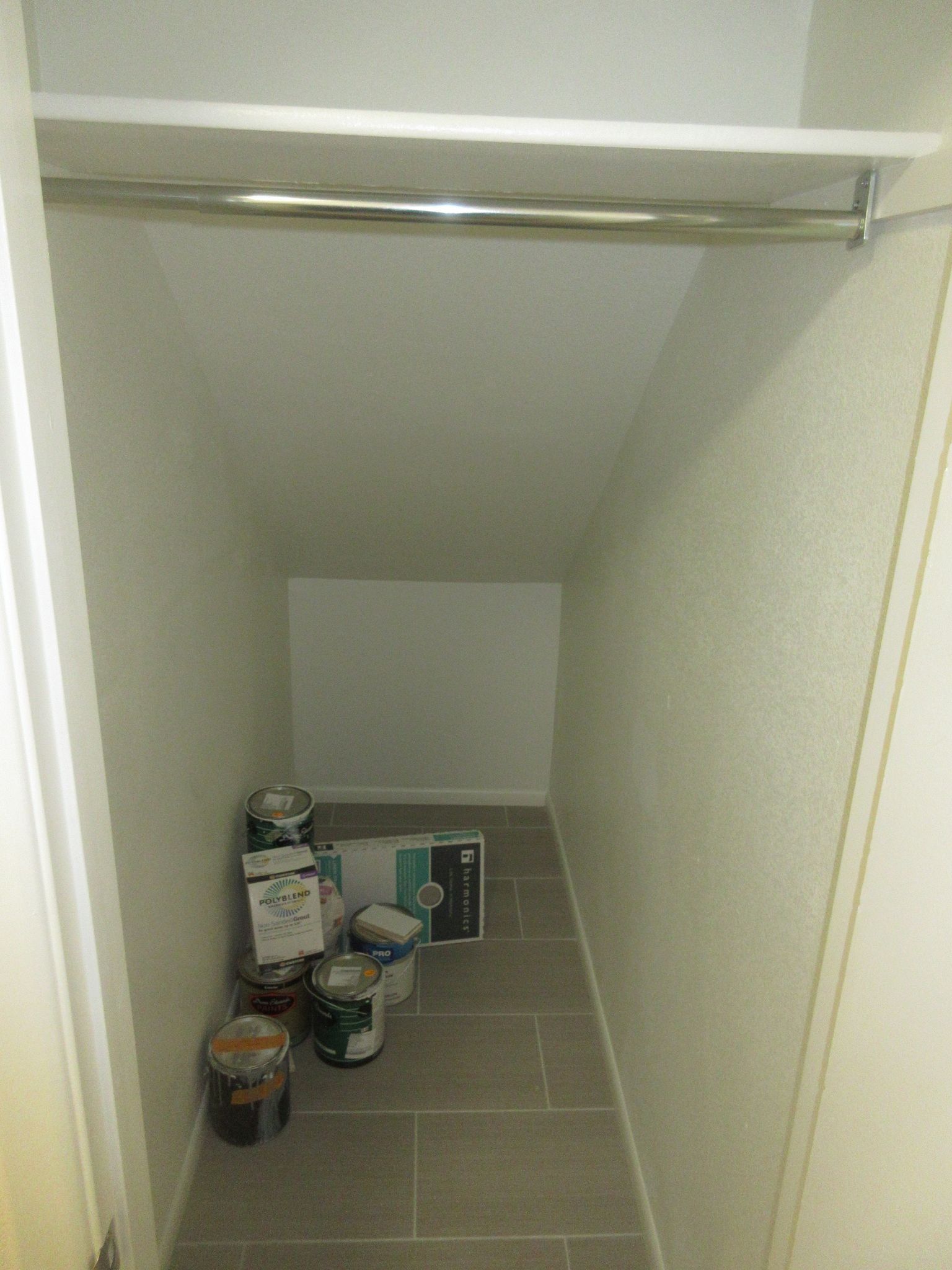 A closet under a staircase with buckets of paint on the floor.
