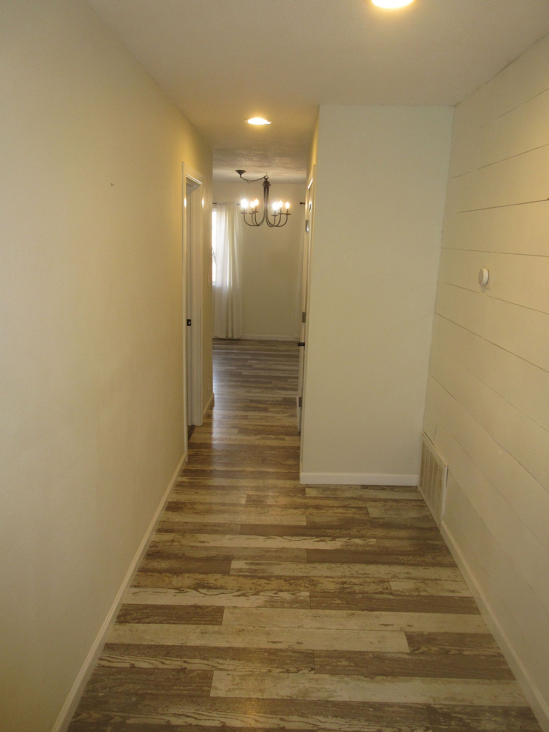 A hallway with wooden floors and white walls leading to a dining room.