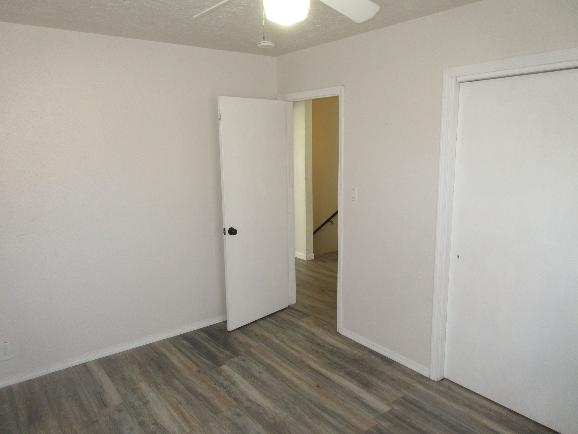 An empty bedroom with a ceiling fan and wooden floors.
