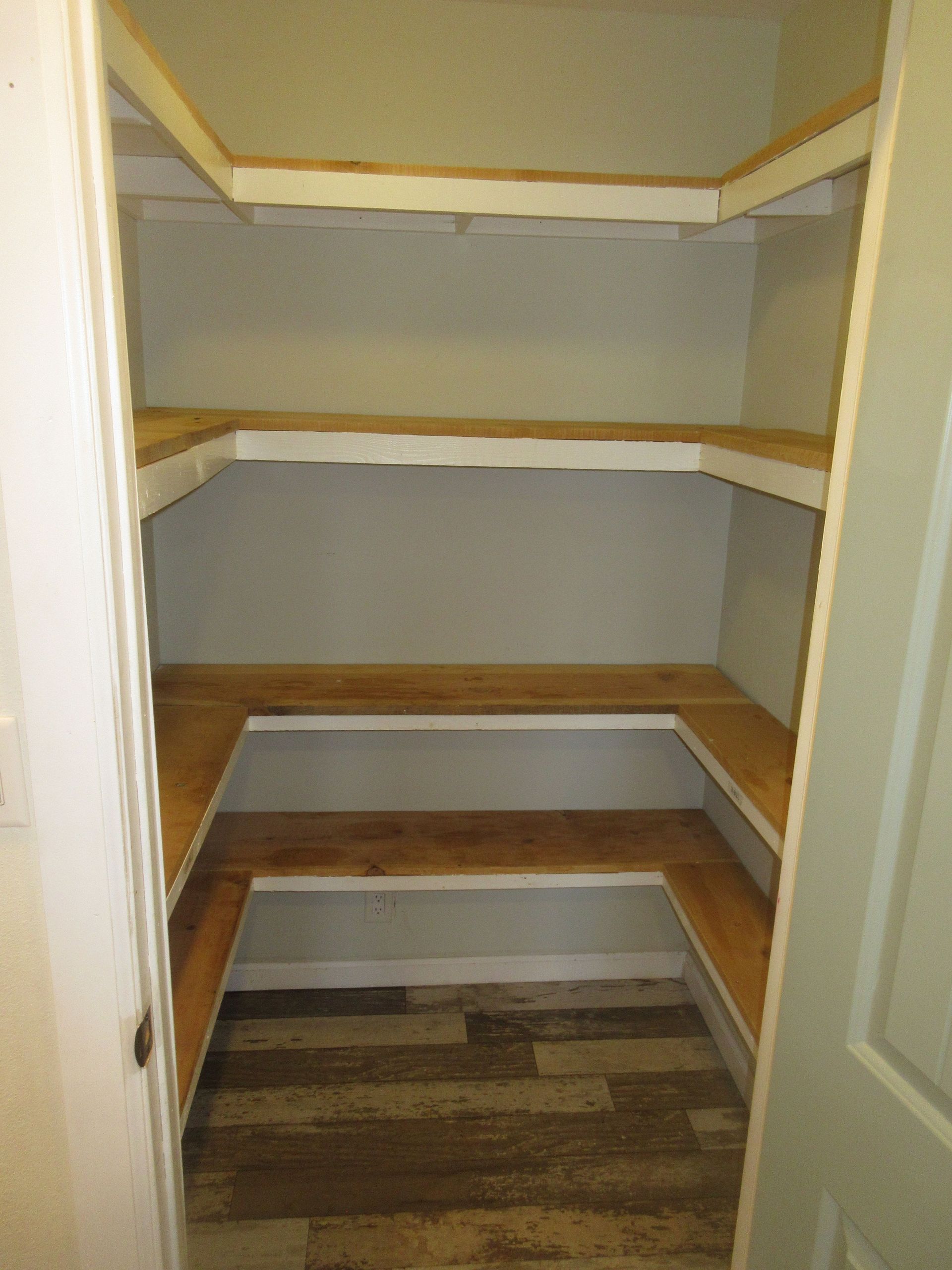 A walk in pantry with wooden shelves and a striped floor.