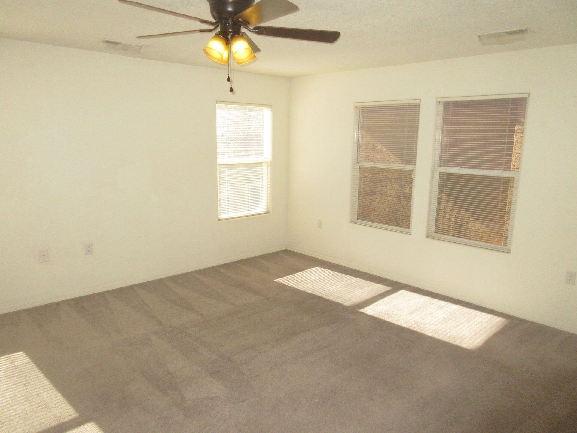 An empty room with a ceiling fan and two windows
