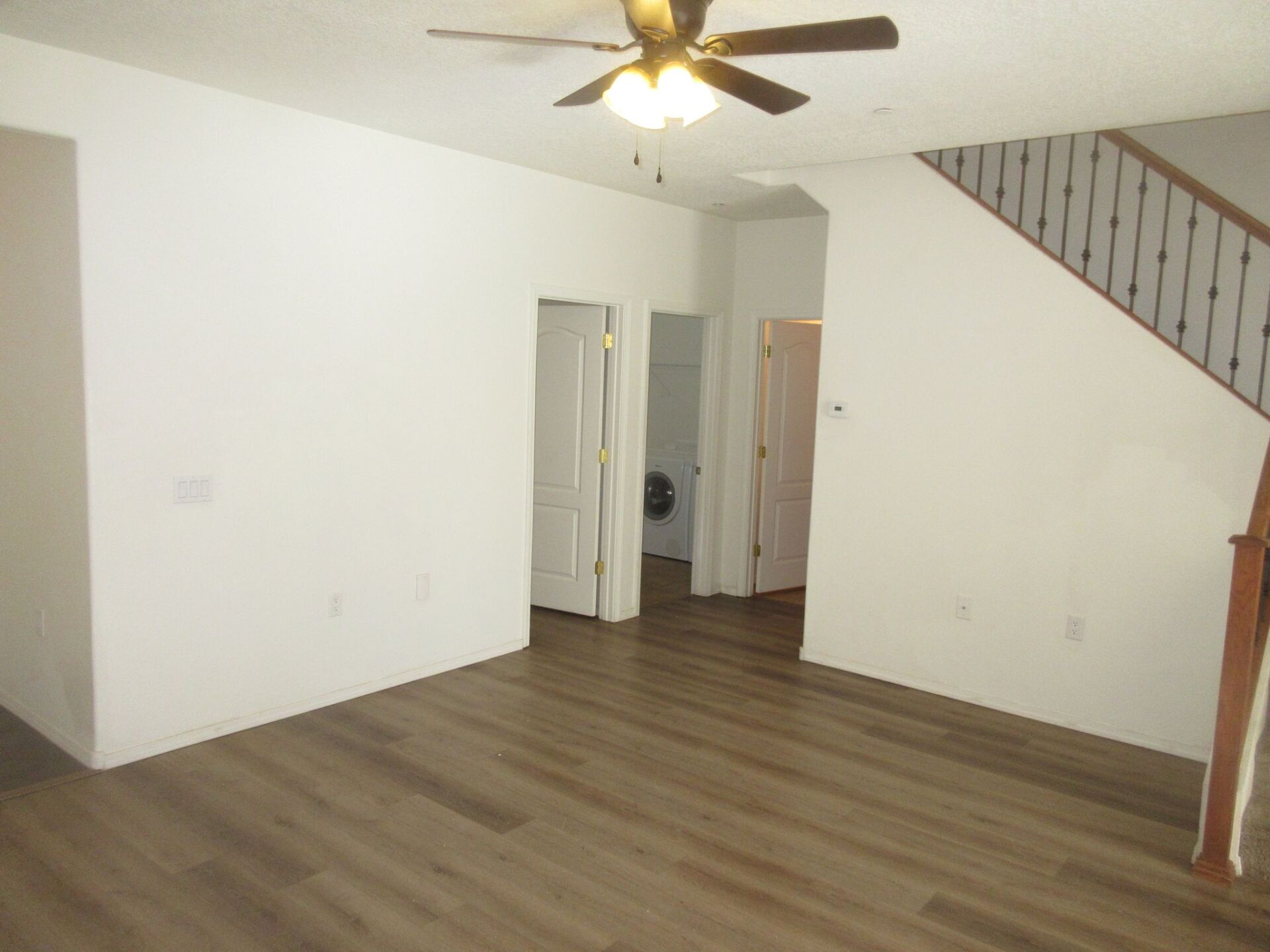 An empty living room with hardwood floors and a ceiling fan