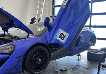 Blue race car with door open, being worked on inside a garage.