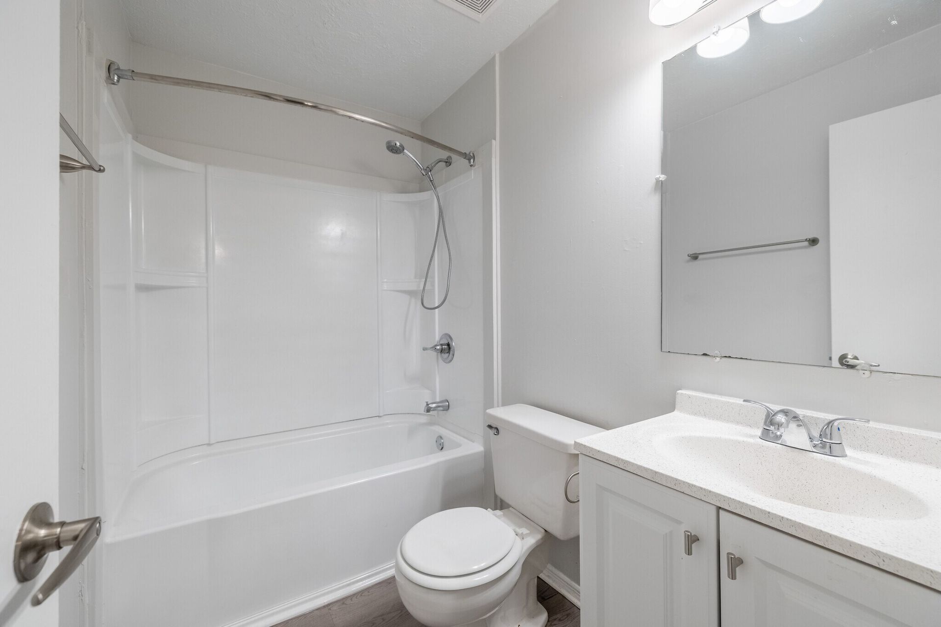 White bathroom with tub/shower, toilet, vanity, and a large mirror at  Glastonbury Woods Apartments.