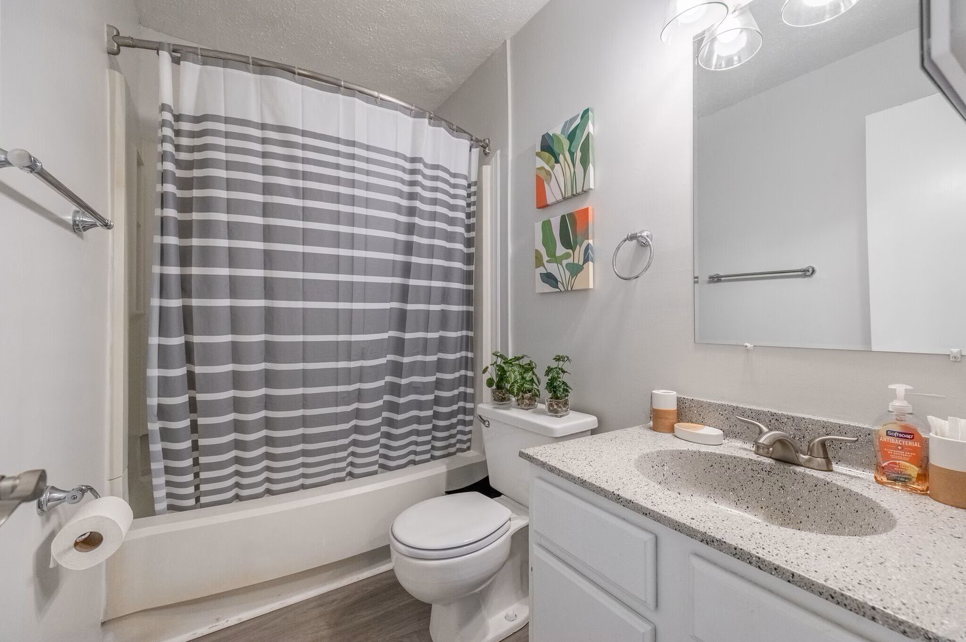 Bathroom with gray and white striped shower curtain, white vanity, and small plants at  Glastonbury Woods Apartments.