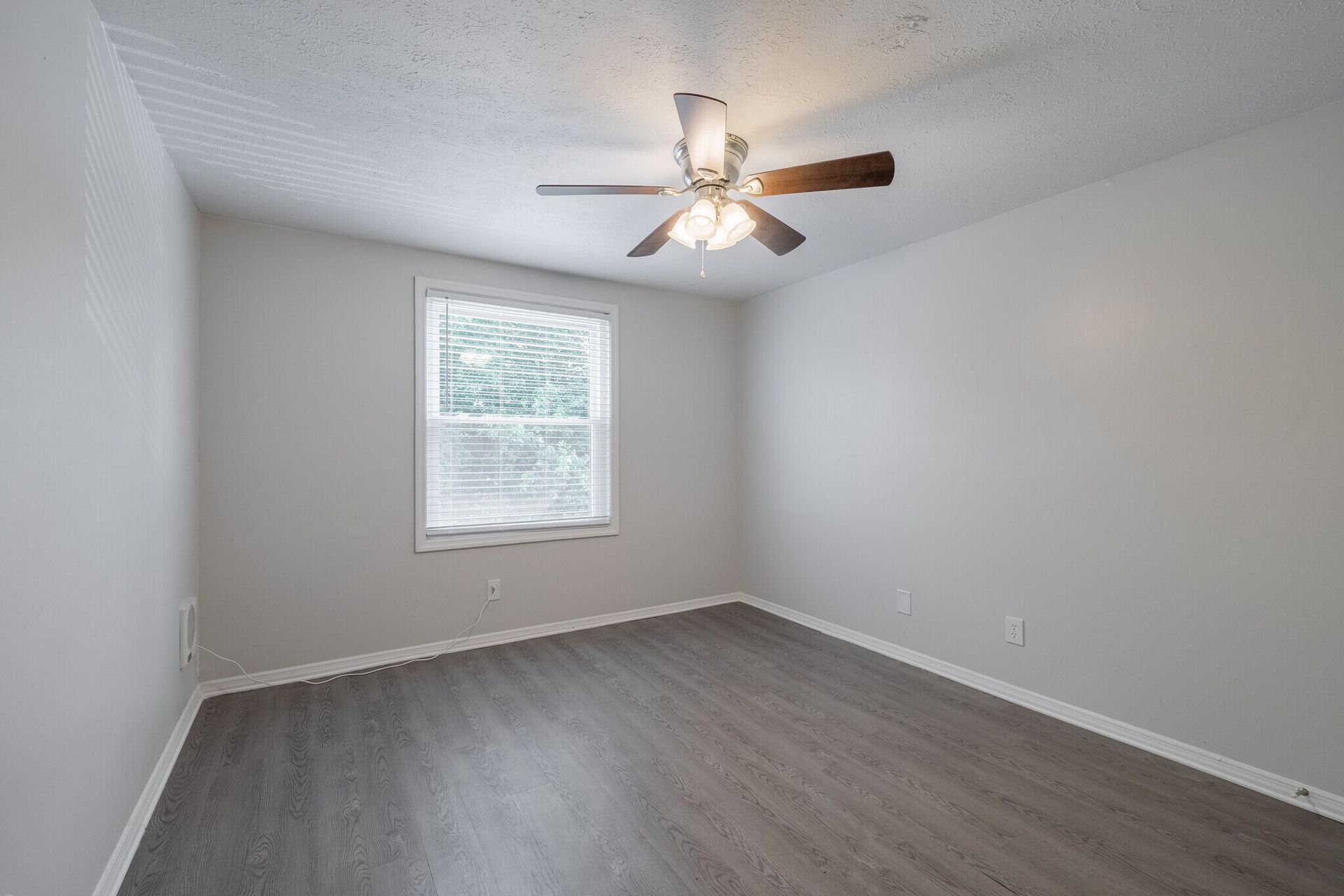 Empty bedroom with gray walls, wood-look floor, window, ceiling fan at  Glastonbury Woods Apartments.