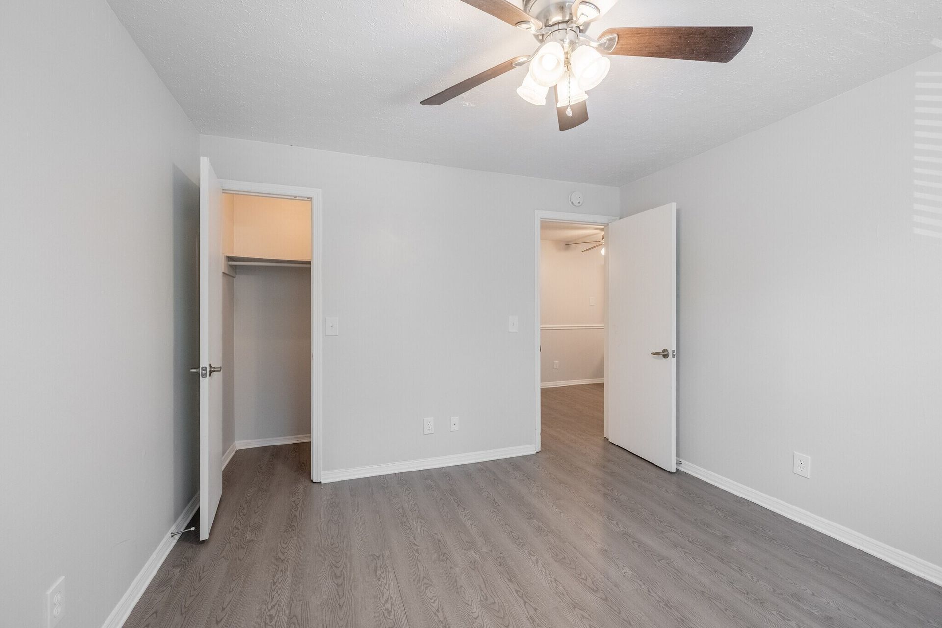 Empty bedroom with gray walls, wood-look flooring, ceiling fan, open closet, and two open doors at  Glastonbury Woods Apartments.
