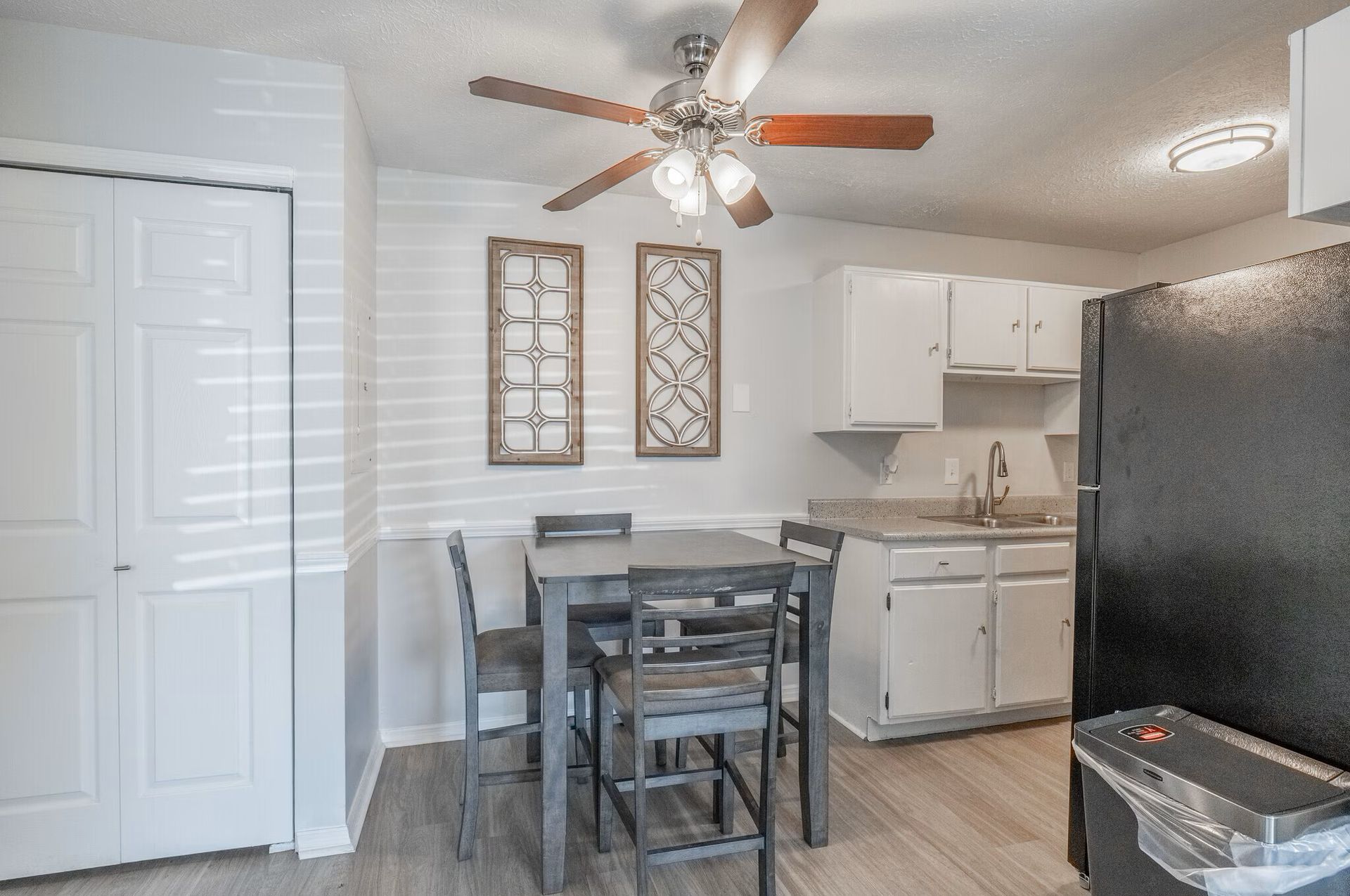 A small kitchen at  Glastonbury Woods Apartments with a dining table, white cabinets, and a black refrigerator.