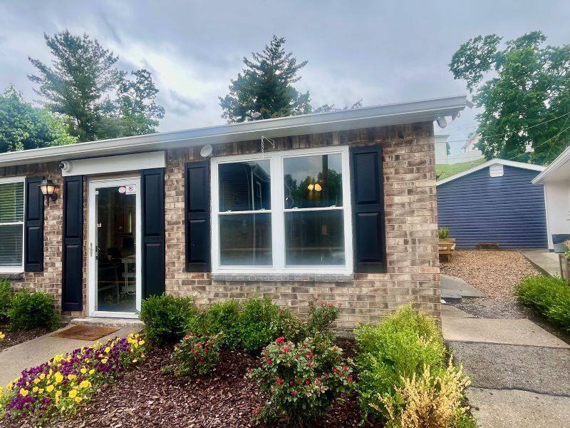 Brick house with black shutters, white-framed window, and a door, with landscaping in front at  Glastonbury Woods Apartments.