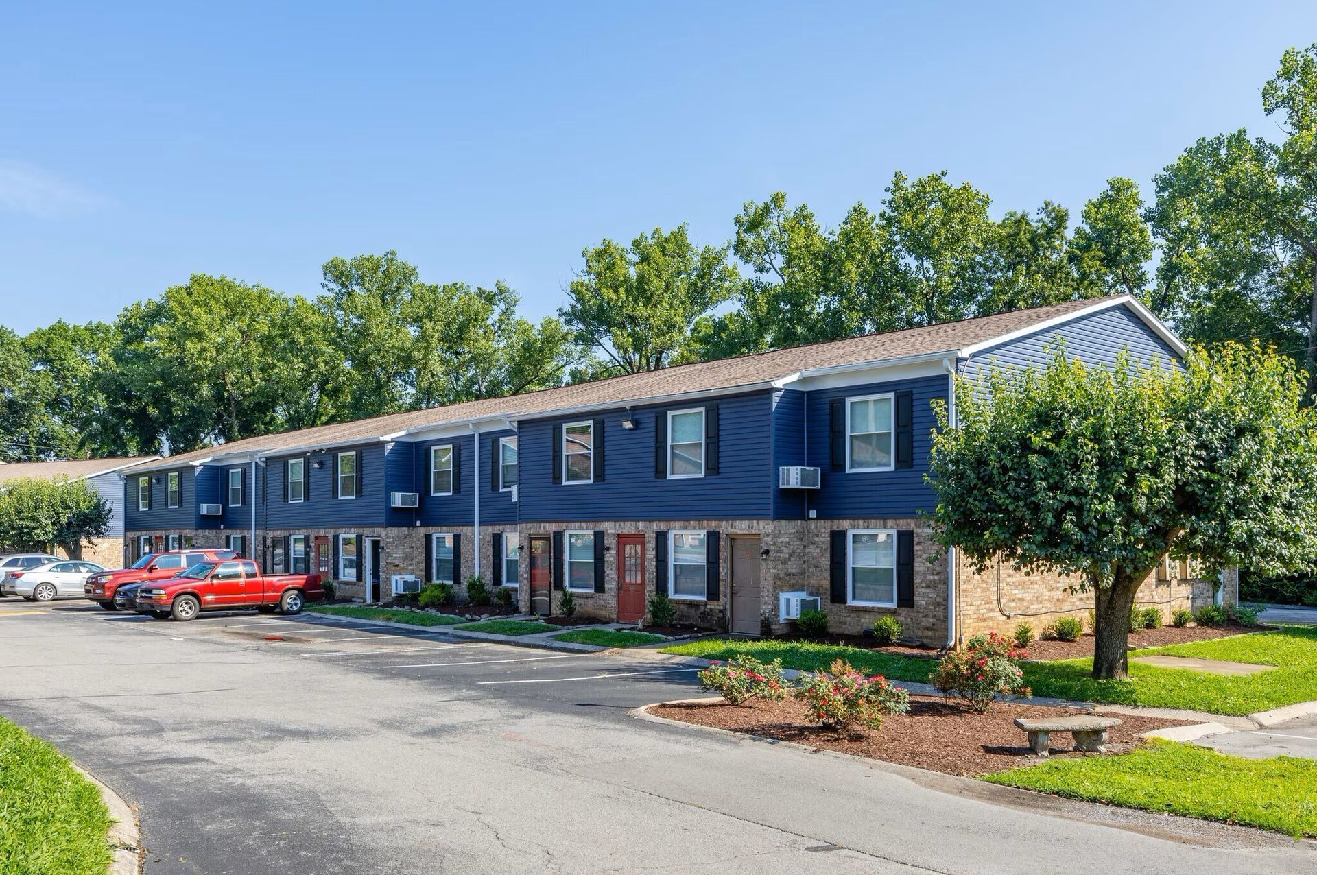 Blue two-story apartment building at  Glastonbury Woods Apartments with black shutters and a red car parked out front.