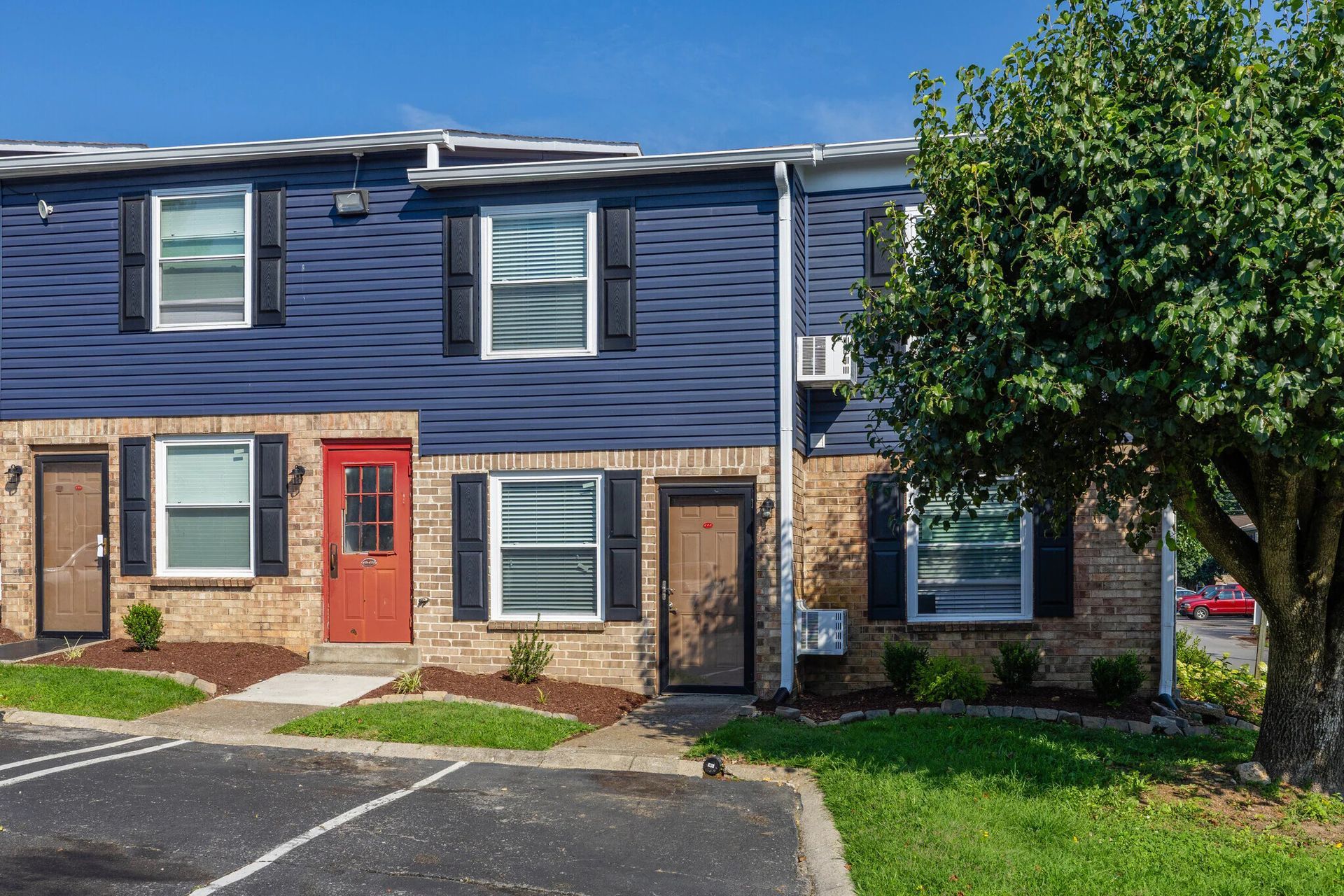Two-story townhouses with blue siding, brick base, black shutters, and red front door at Glastonbury Woods Apartments.