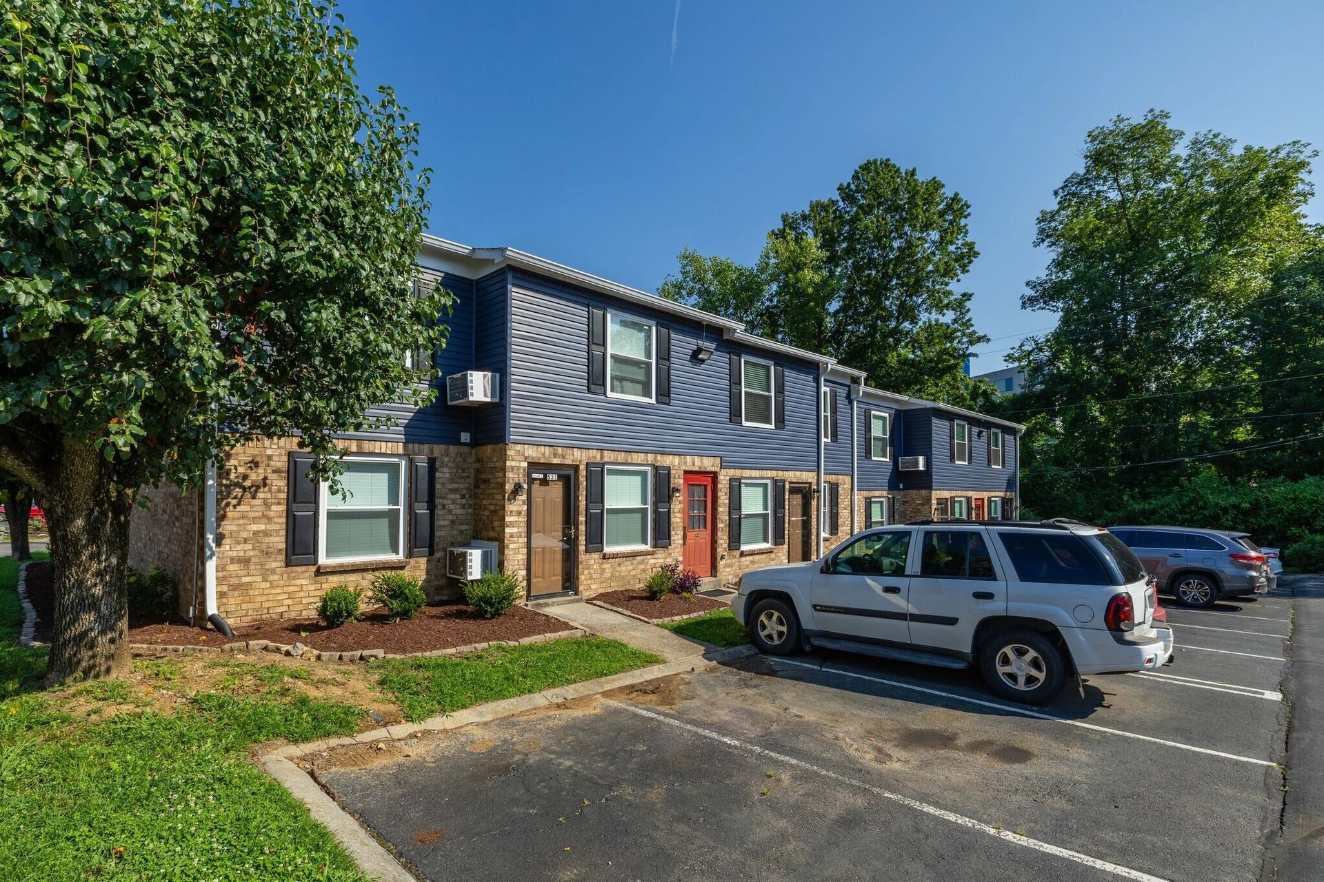 Blue and brick apartment building with parking, a silver SUV is parked in front at  Glastonbury Woods Apartments.