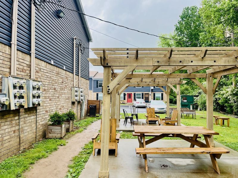 Glastonbury Woods Apartments outdoor seating area with pergola, picnic table, and chairs. Buildings and trees in background.