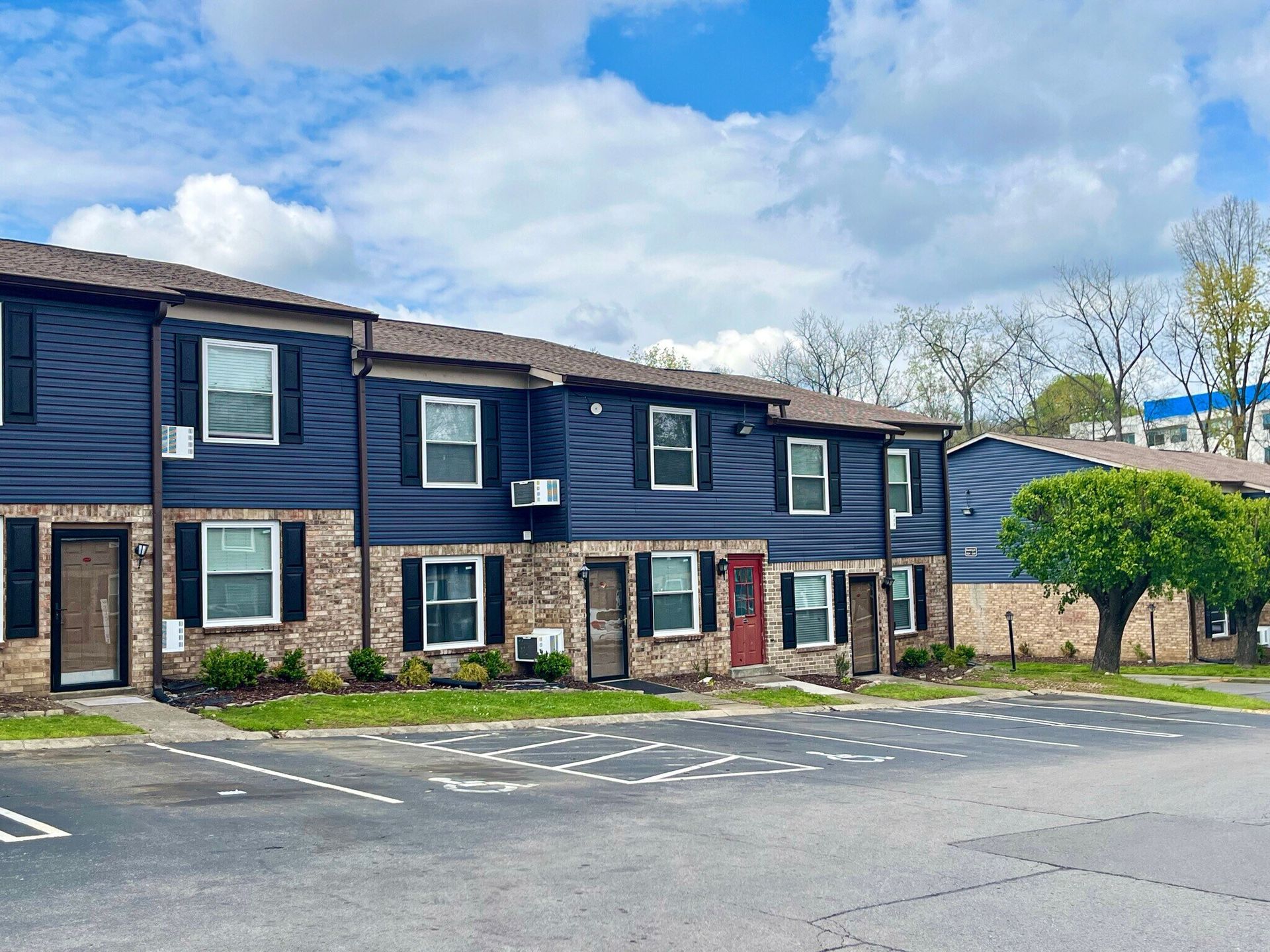 Multi-unit, two-story apartments with dark blue siding, brick accents, and a parking lot at Glastonbury Woods Apartments.