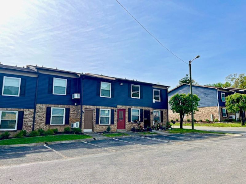 Blue and brick townhouses at Glastonbury Woods Apartments with parking spaces on a sunny day.