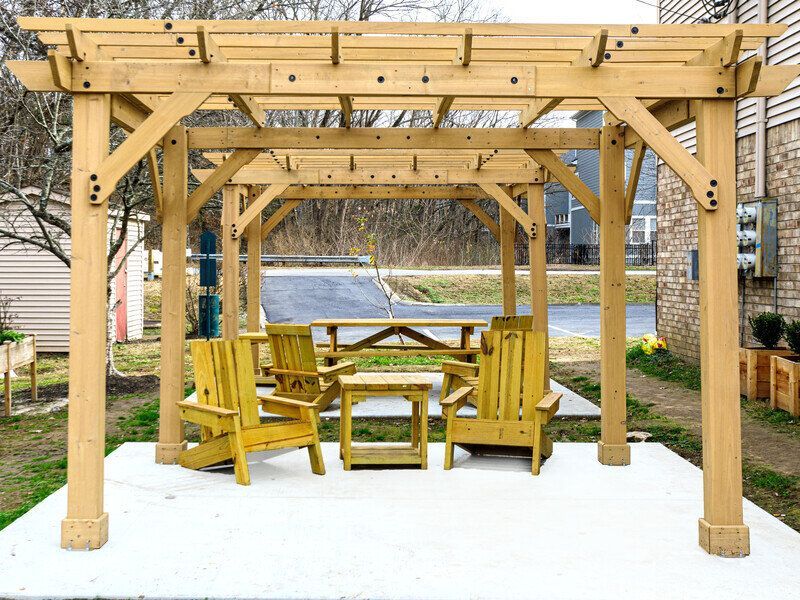 Wooden pergola over patio with seating: Adirondack chairs, small table, picnic table at  Glastonbury Woods Apartments.