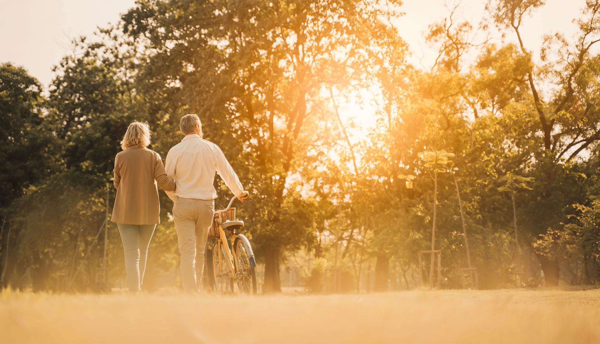 a man and a woman are walking in a park with a bicycle .