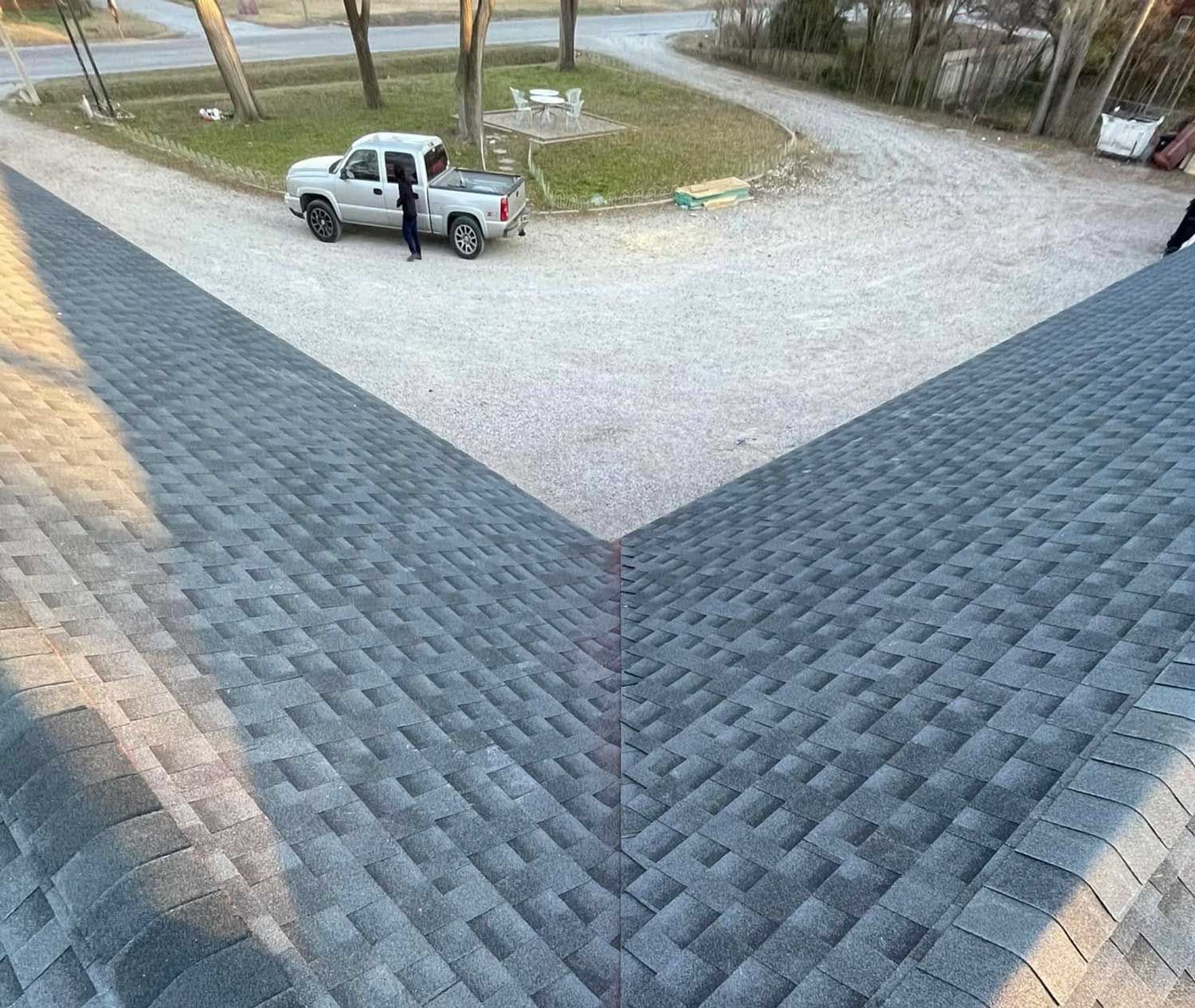 Overhead view of gray shingle roof, person near a truck on gravel drive.
