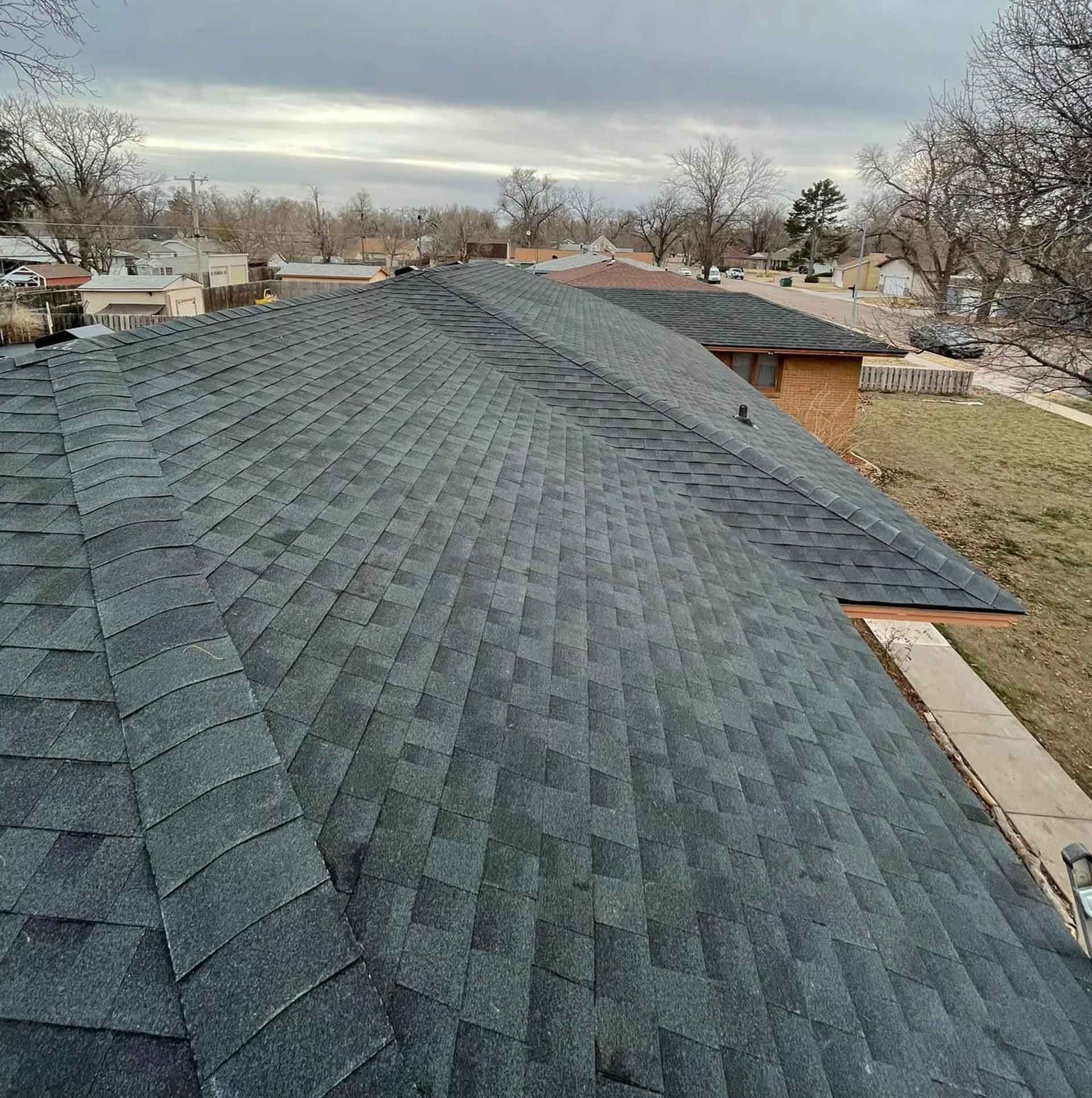 Gray asphalt shingle roof on a residential building under a cloudy sky.