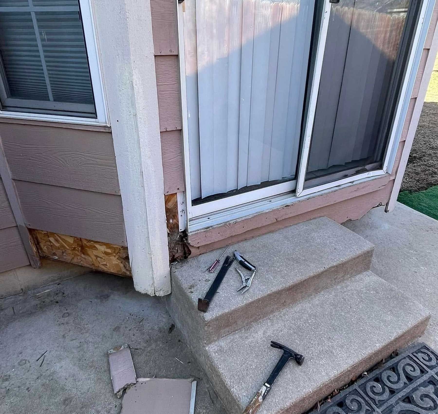 Damaged exterior wall next to a sliding door and steps with tools on the stairs.