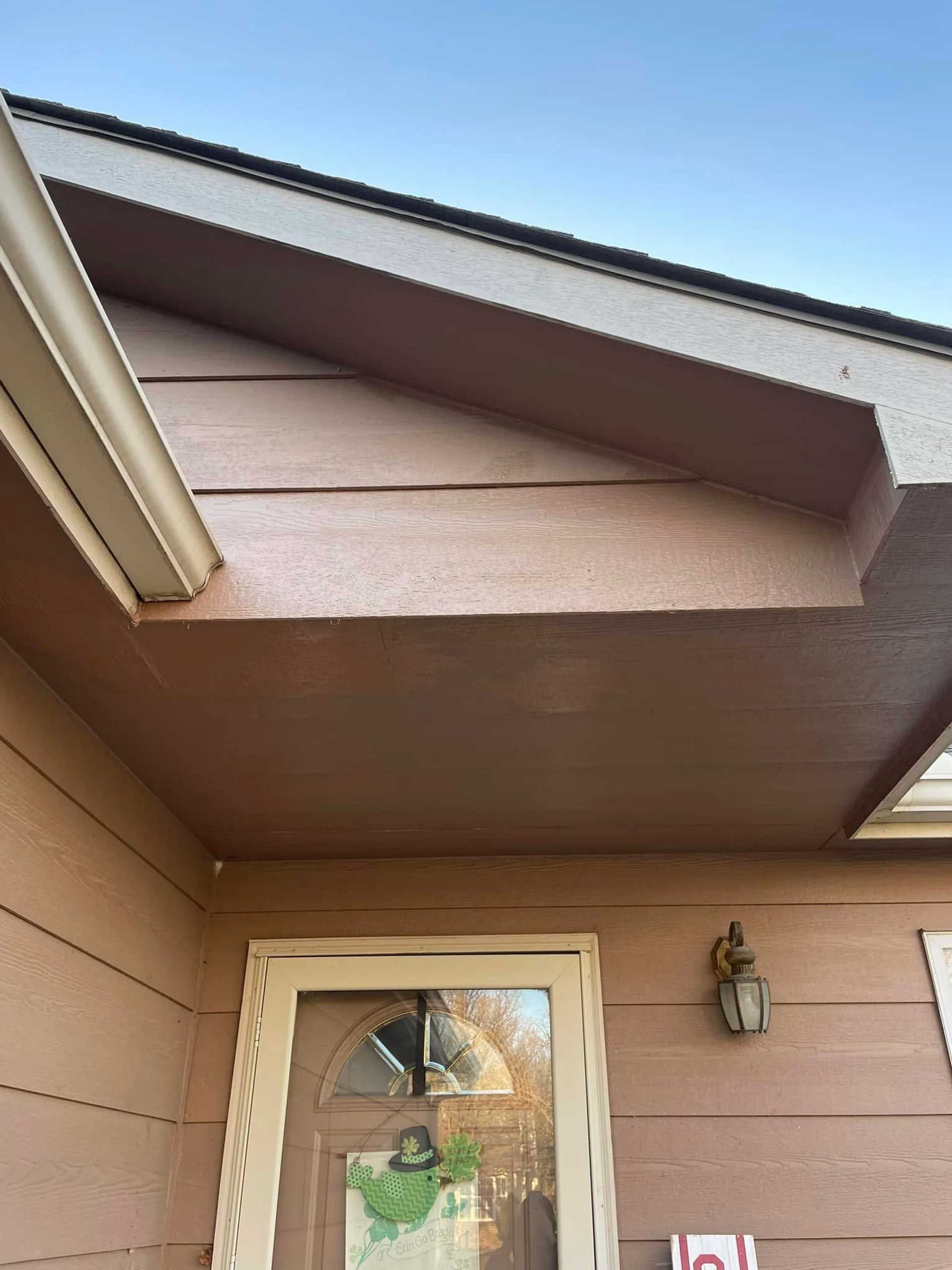 Brown house exterior with covered porch, door, and a light fixture.