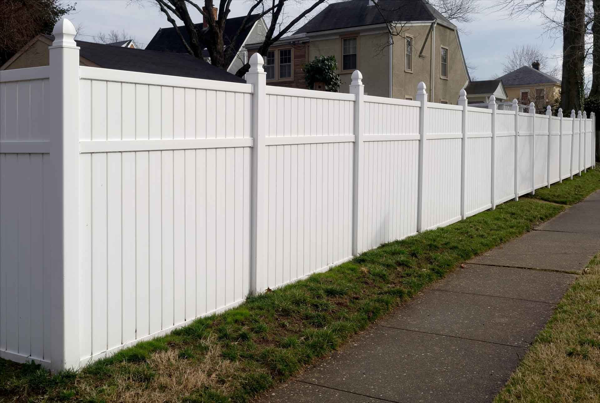White vinyl fence along a sidewalk, separating the road from houses.