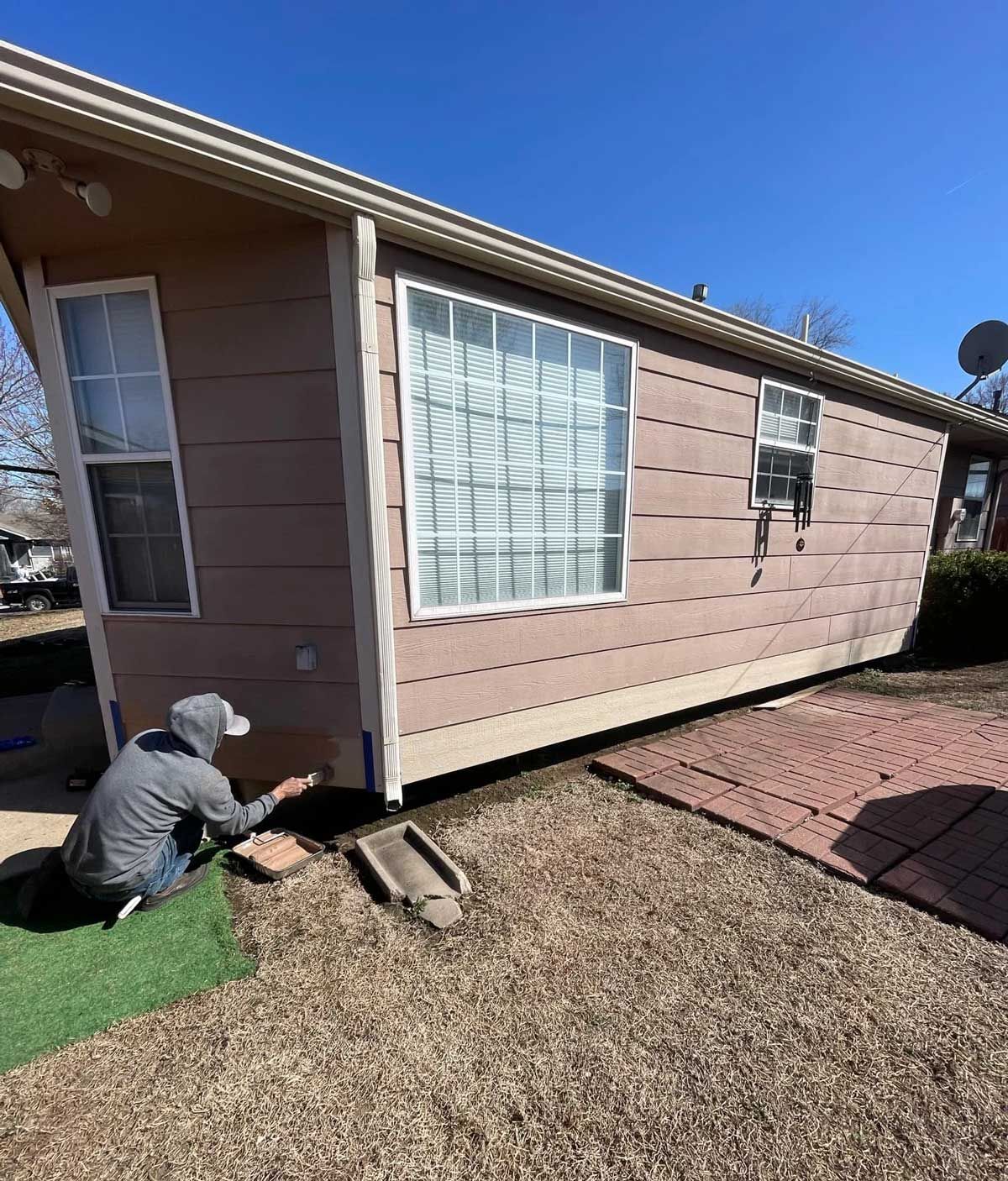 Person installing pavers near a house with pink siding.