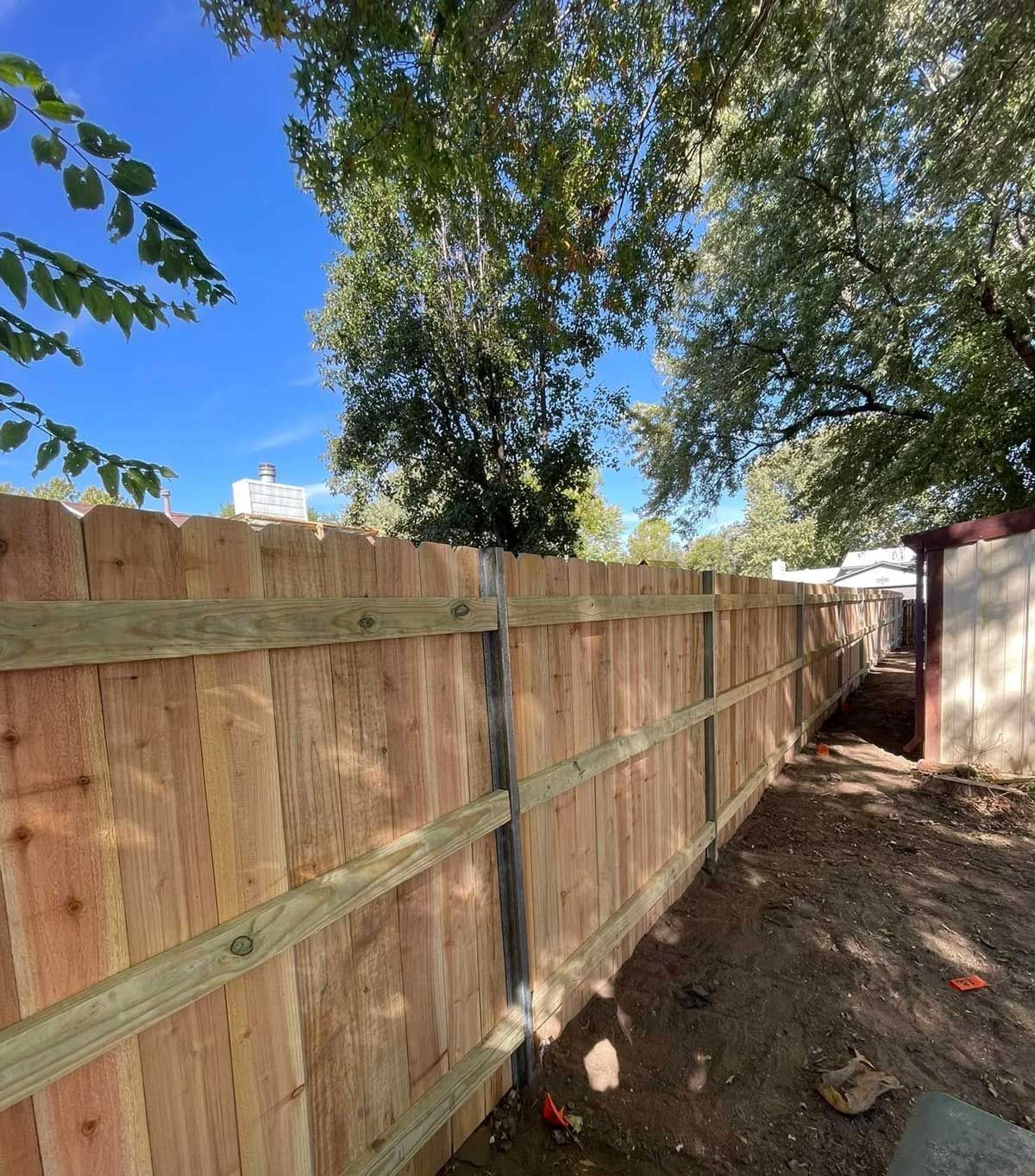 Wooden privacy fence in a yard with trees under a blue sky.