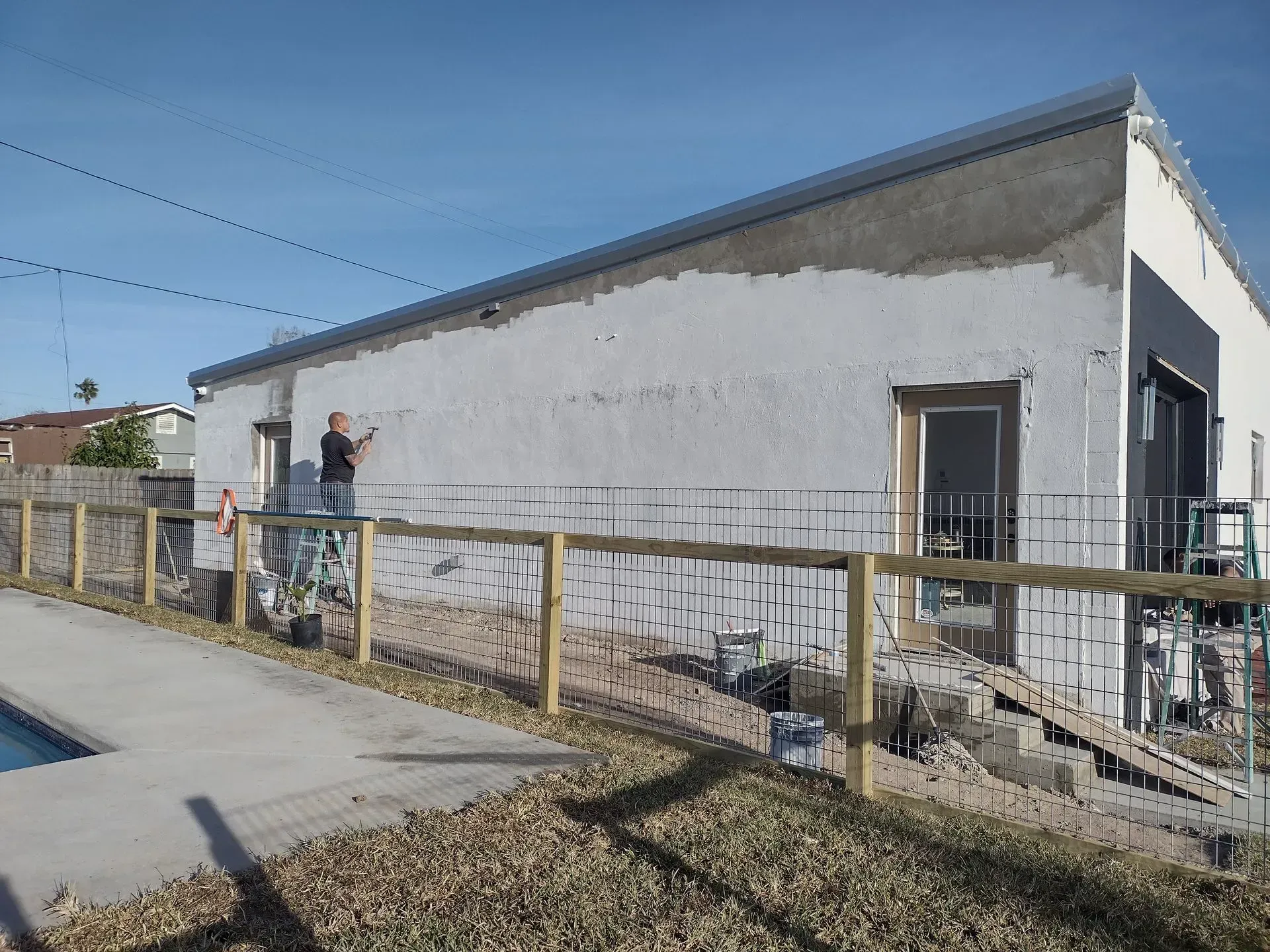 a man is painting a white building with a wooden fence in front of it