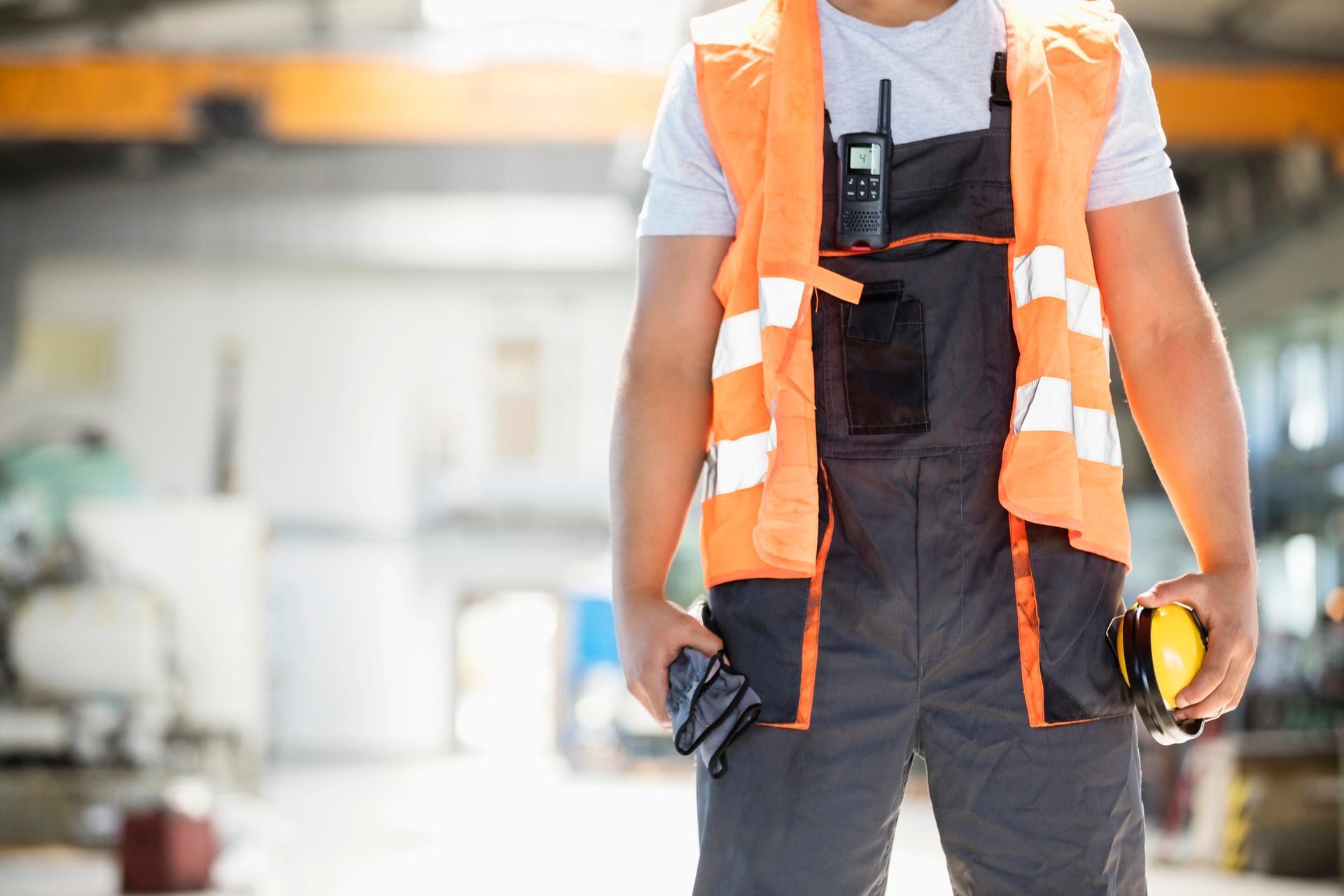 Un trabajador de la construcción que viste un chaleco y un mono de color naranja sostiene una cinta métrica y un walkie talkie.