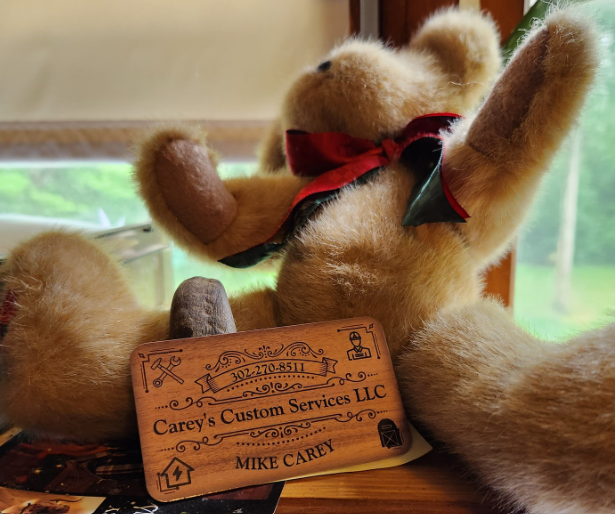 A teddy bear is sitting next to a card that says carey 's custom services llc
