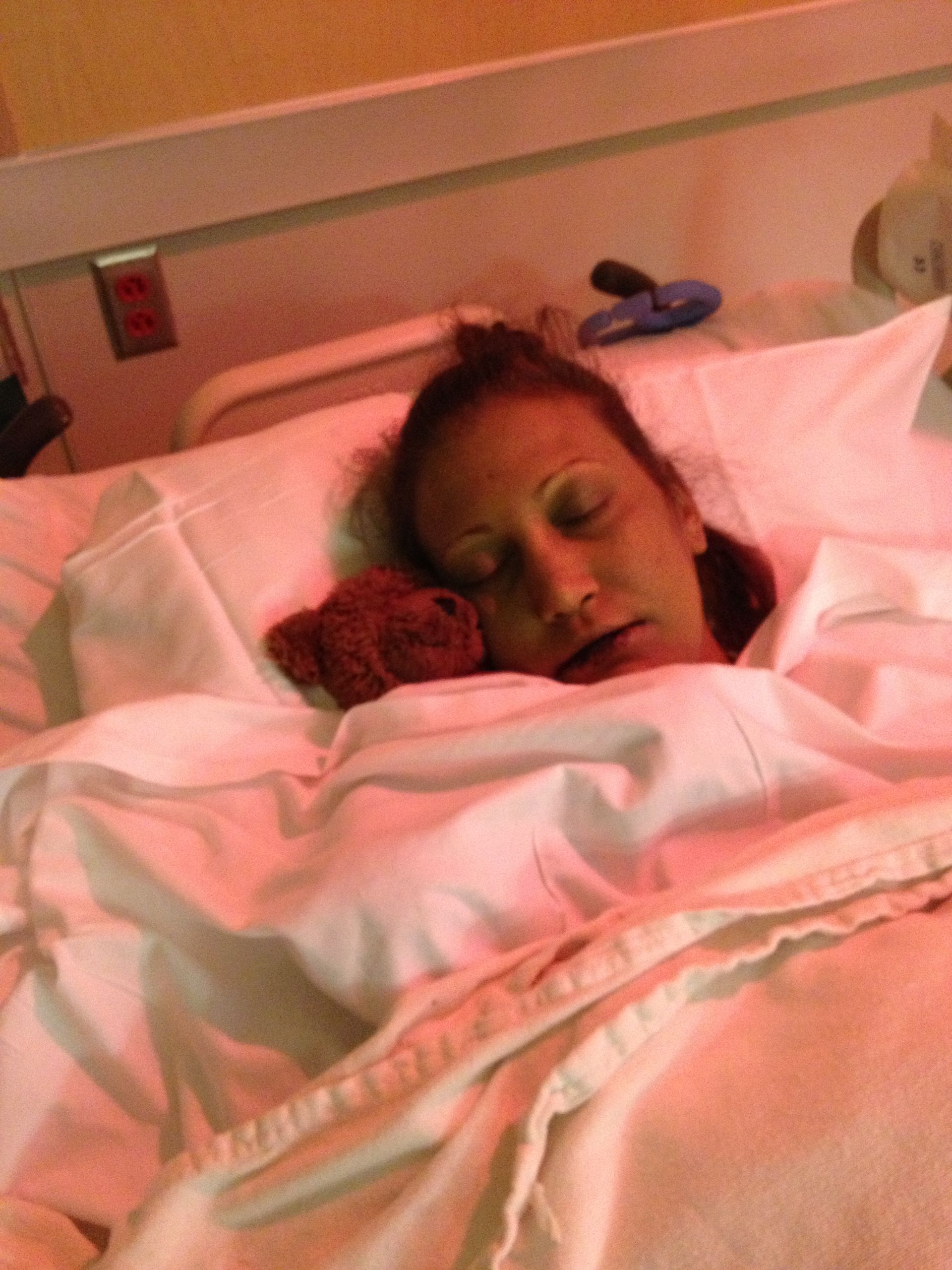 A woman is sleeping in a hospital bed with a teddy bear