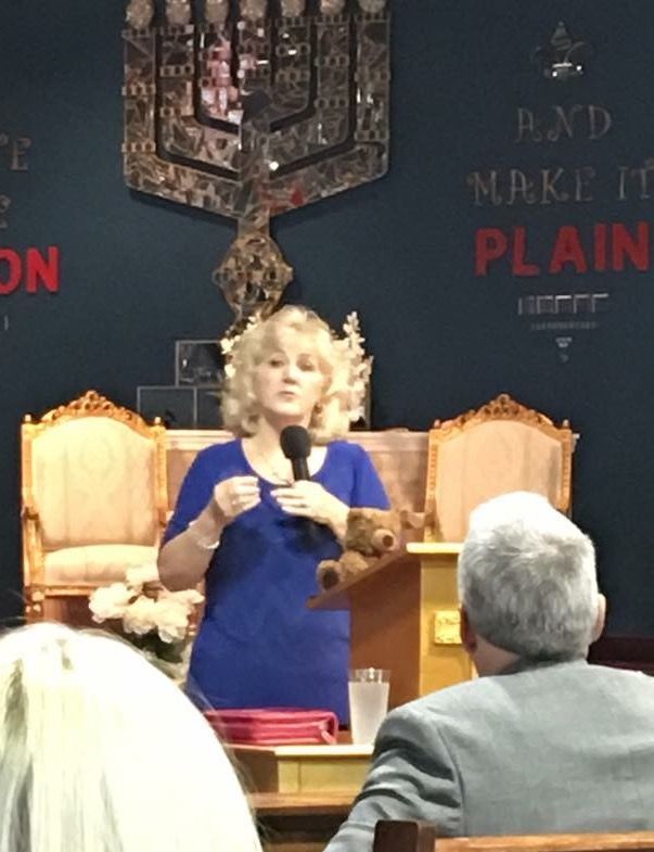 A woman is giving a speech in front of a sign that says make it plain