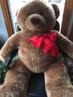 A brown teddy bear with a red bow is sitting in a chair.
