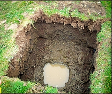Technician inspecting an open lawn access hole beside tools in a landscaped yard with mountains in the background