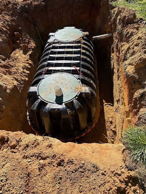 Worker kneeling over a green septic tank lid in a landscaped yard beside a service truck