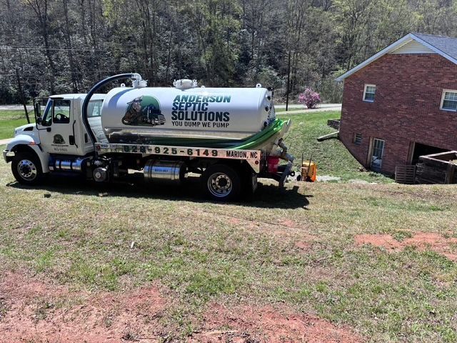 Worker installing white PVC pipes in a dirt trench beside a landscaped yard