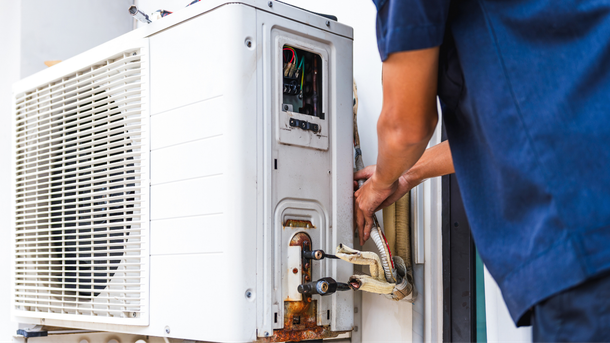 HVAC technician repairing an outdoor air conditioning unit.