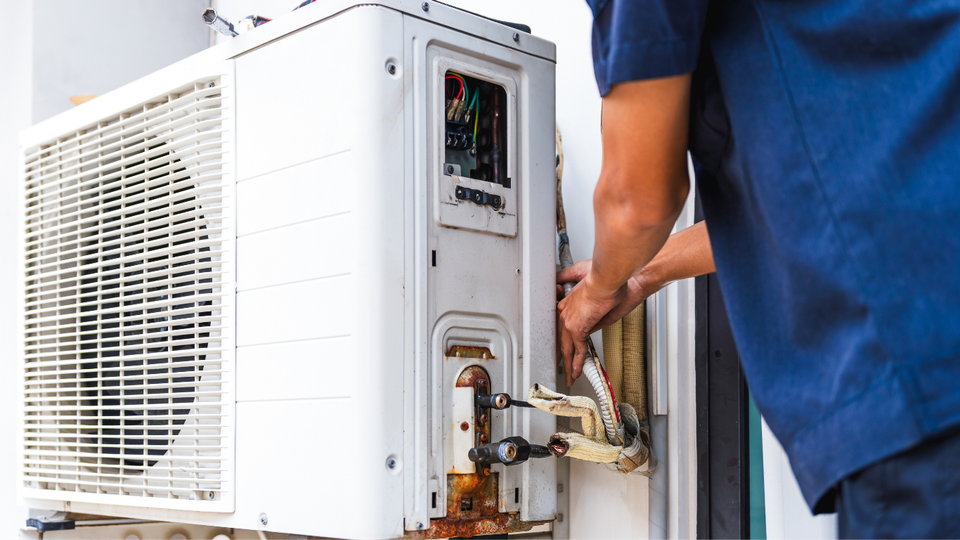 Person in blue shirt repairing an outdoor air conditioning unit.