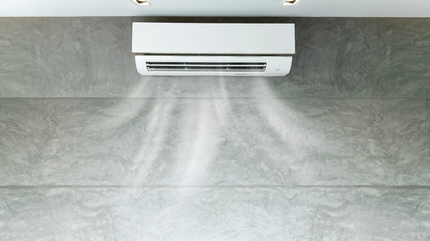 White air conditioner blowing cool air on a gray, concrete wall.
