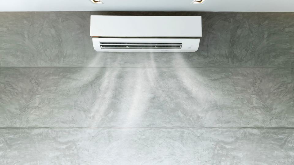 White air conditioner blowing cool air on a gray wall.