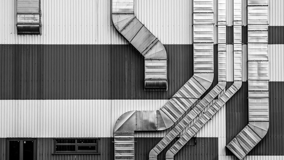 Exterior of a building with multiple metal ventilation ducts running down the striped wall.