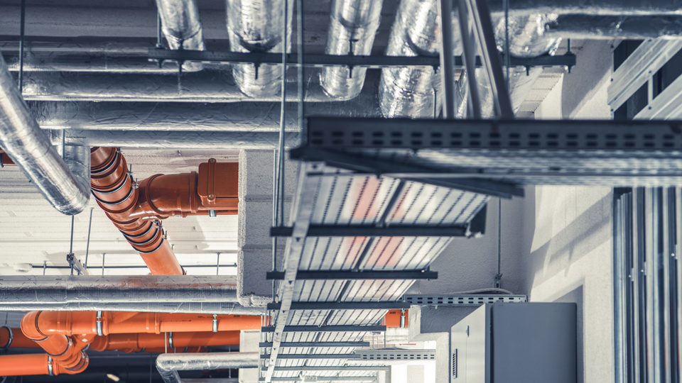 Orange pipes, silver ductwork, and cable trays in an industrial ceiling.