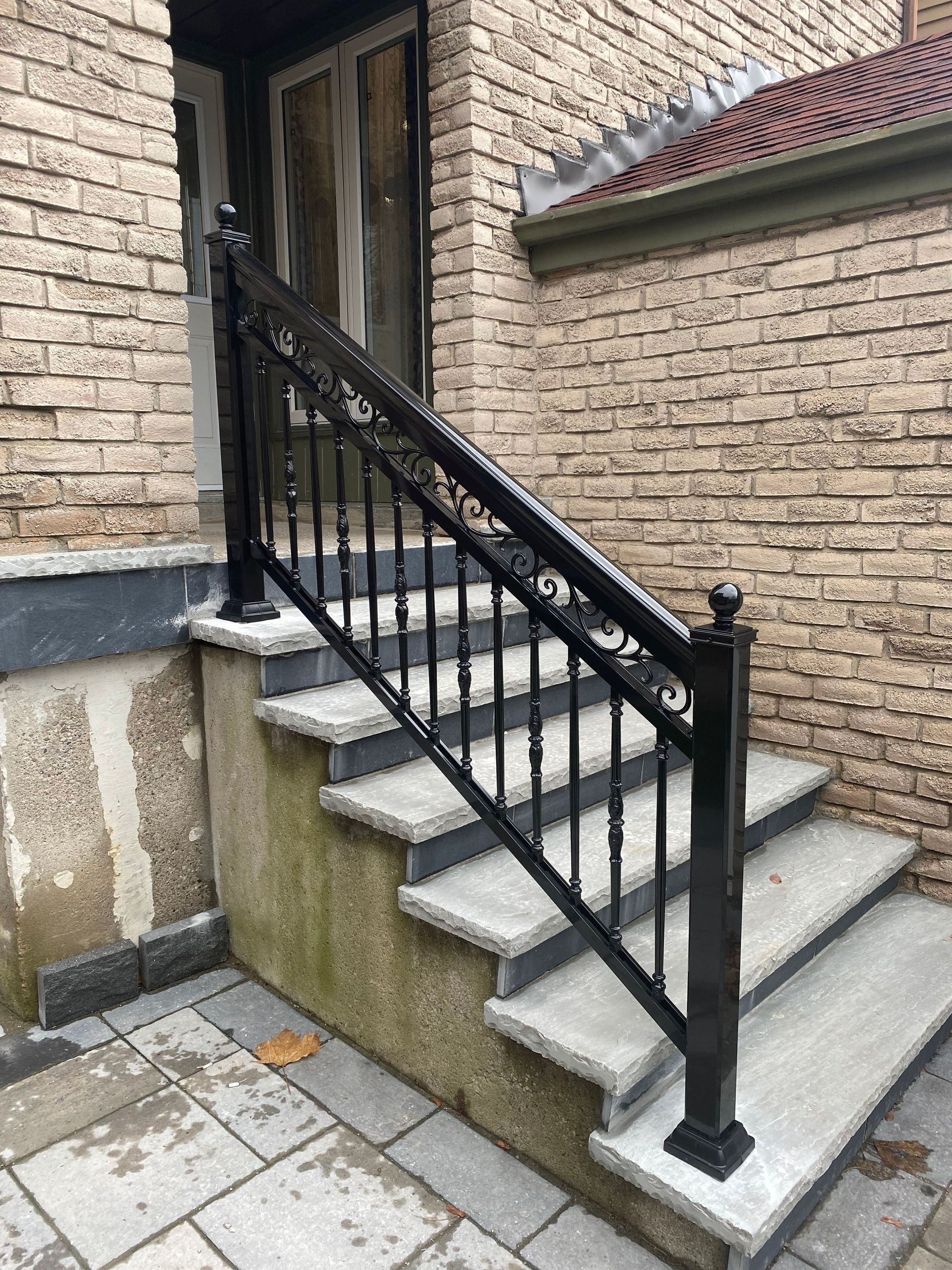 Black wrought-iron handrail on concrete steps leading to a doorway. Brick wall backdrop.