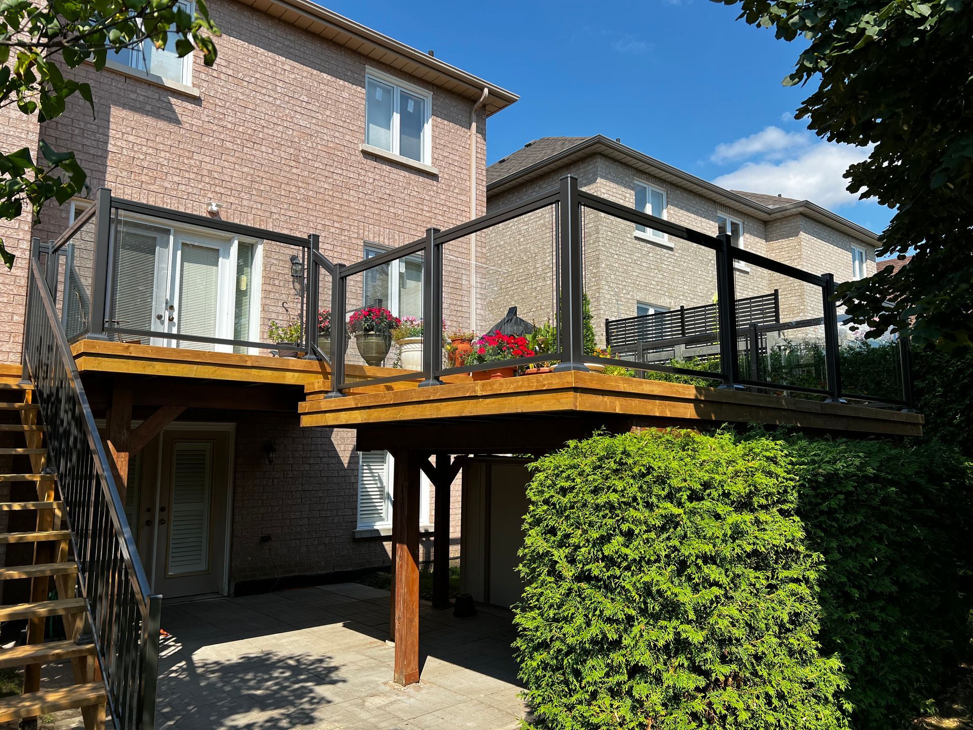 Elevated wooden deck with black aluminum and glass railing, featuring patio furniture.