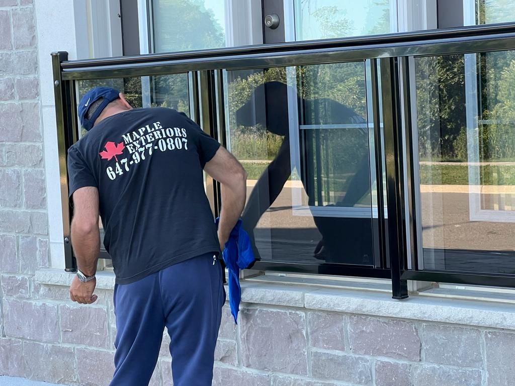 Worker cleaning a glass railing installation on a residential exterior wall.
