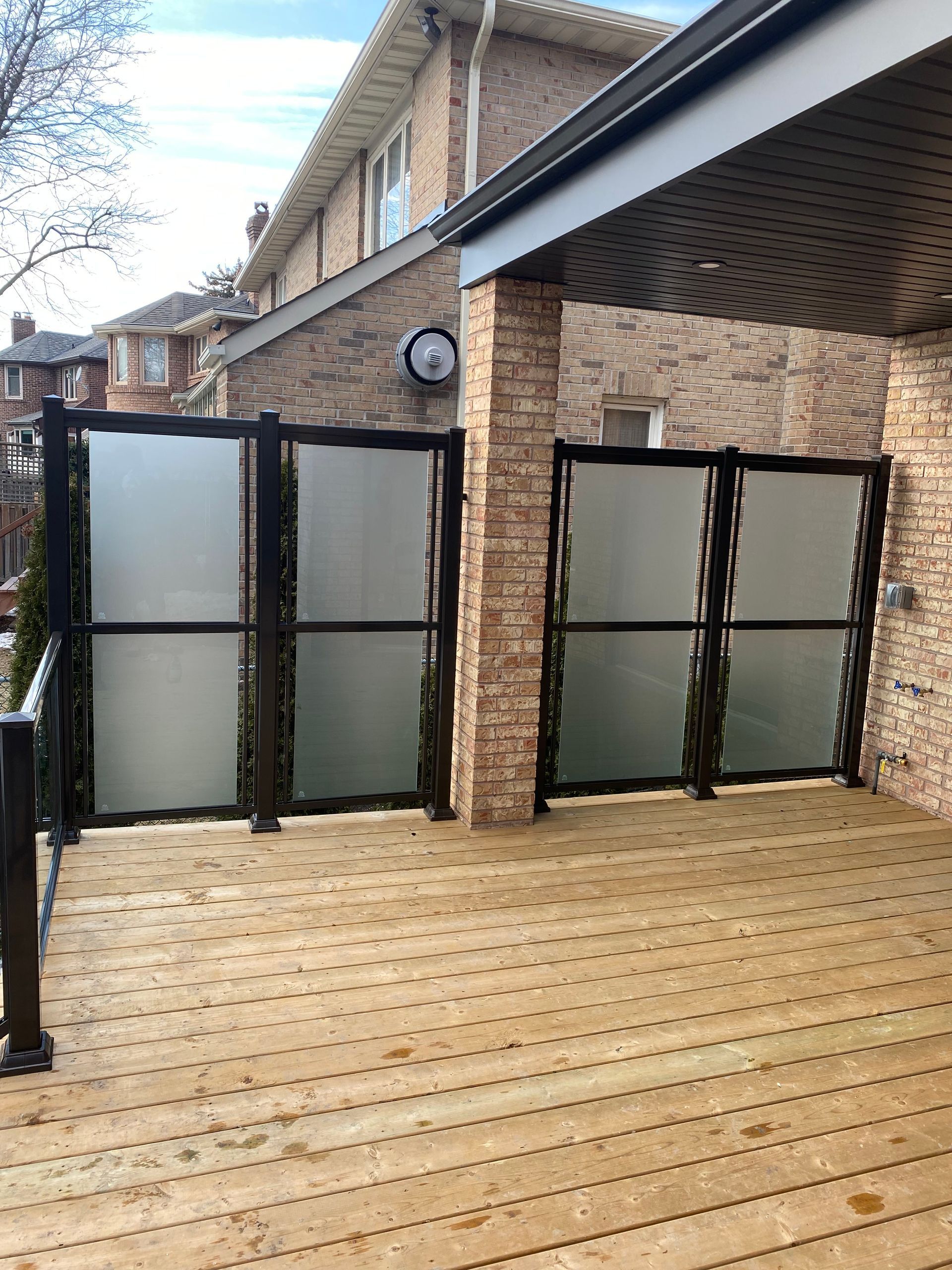 Wooden deck with frosted glass panels, brick columns, and a view of a brick house.