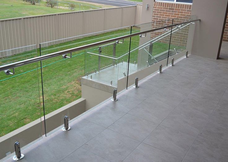 A balcony with a glass railing and a fence in the background.