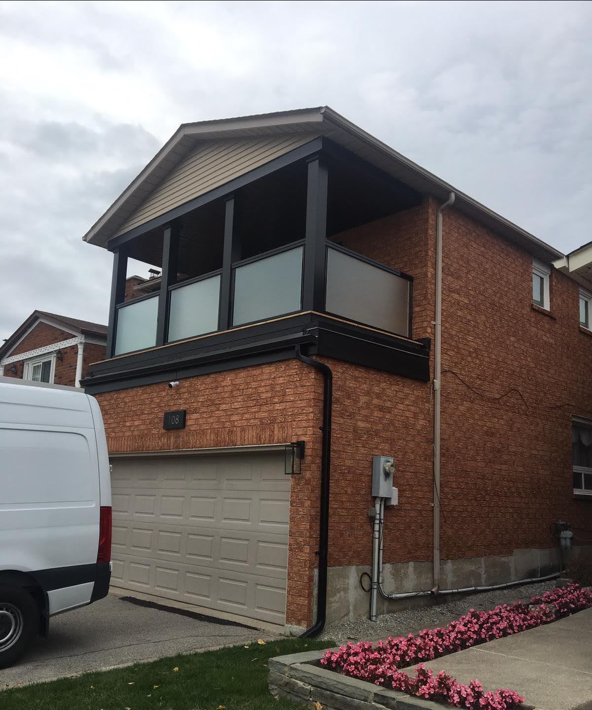 A white van is parked in front of a brick house with a balcony.